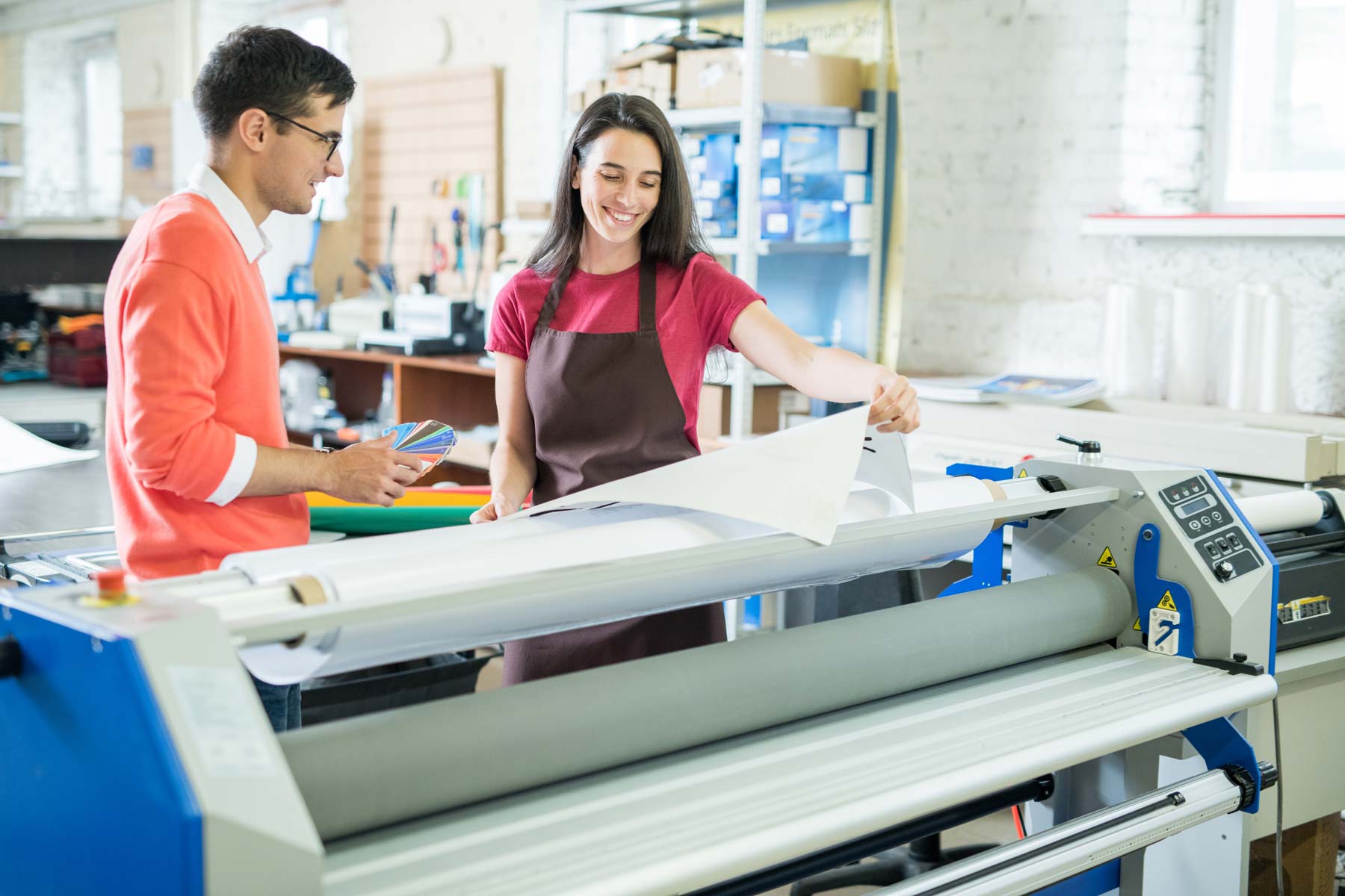 Two people working with large paper roll on a machine in a print workshop setting.